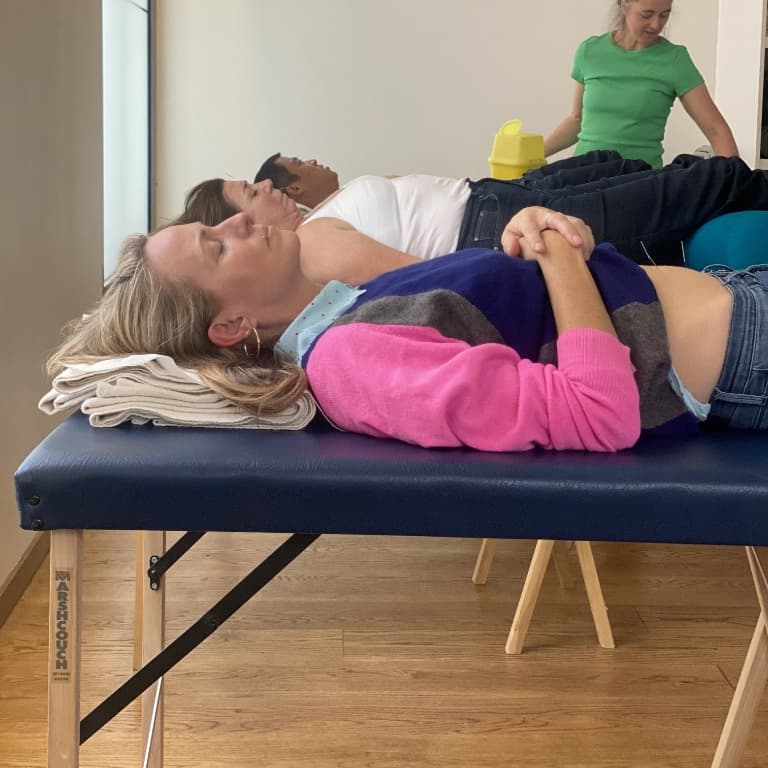 3 patients lying on treatment tables peacefully relaxing during their acupuncture treatments at The Get Well Clinics. In the background an acupuncturist in a green top is working.