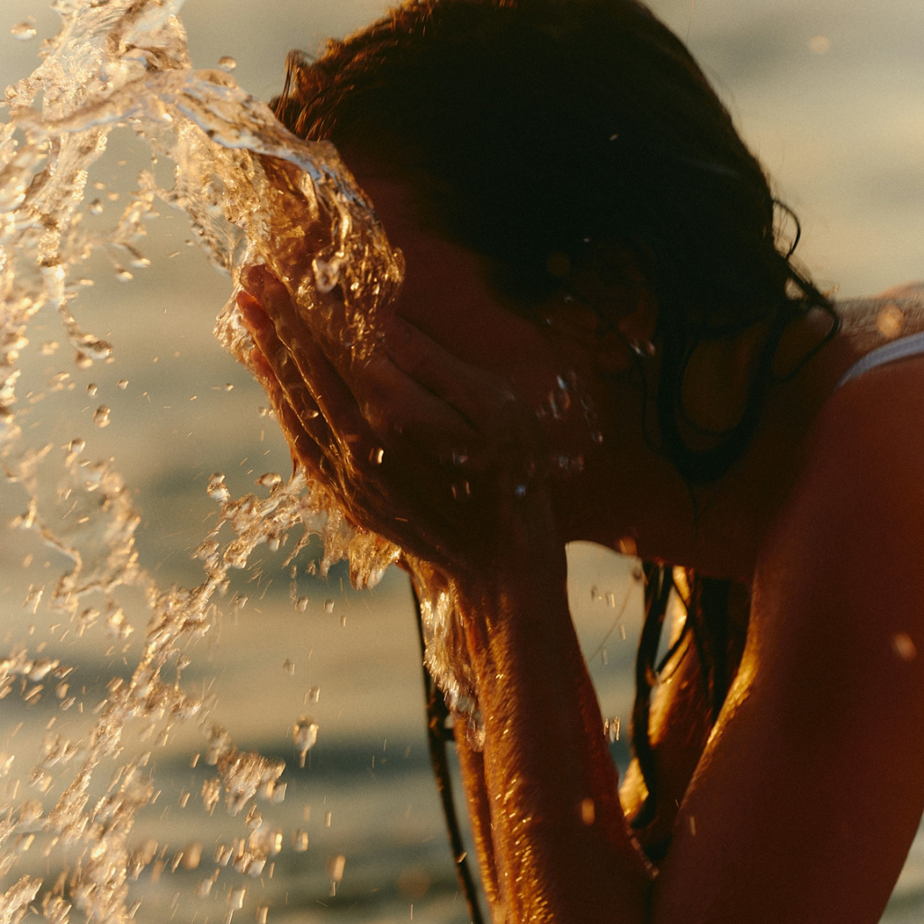 A woman splashes water on her face either from a river or the sea.
