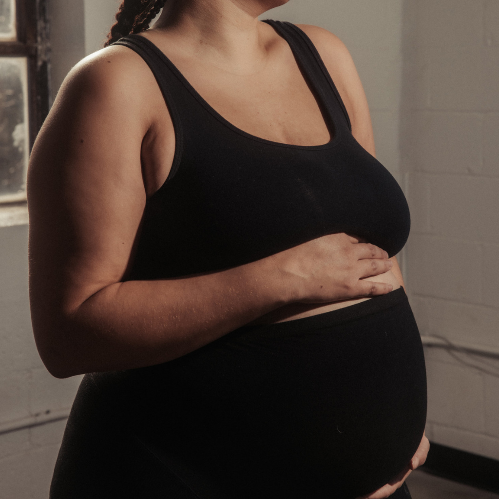 A pregnant woman in a crop top, holds her belly.