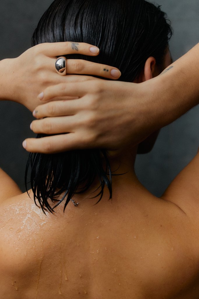 A woman from the back. Her short black hair and back is wet as if she has got out of the shower.