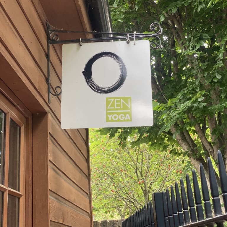 Zen Yoga sign hanging from the wooden cabin building South London, Camberwell. In the background trees in leaf and the edge of the black railings.