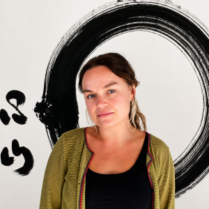 Portrait image of Minnie Casey wearing a black top and green cardigan against a white painting with a black circular brushstroke