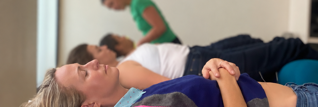 image hero with faces changed a girl in foreground in pink jumper lies on acupuncture table looking rested. in the distance other patients rest and the acupuncturist is standing up at the back treating a patient.